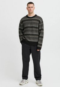 Knit sweater with horizontal black and gray stripes, round neck, and ribbed cuffs, paired with loose black trousers and chunky sneakers.