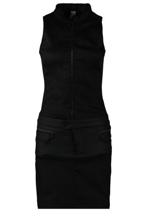 Donkere blauwe denimblouse over een zwarte jurk met rits. Zwarte enkellaarsjes met bandjes en studs. Model loopt en toont de outfit.