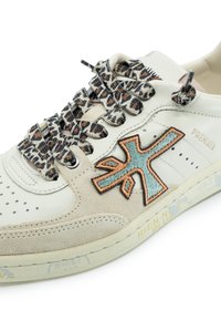 Weiße Leder-Sneaker mit beigen Wildlederakzenten, Schnürsenkeln im Tiermuster und einem gestickten blauen und orangefarbenen Logo. Texturierte Oberfläche und sichtbare Nähdetails.