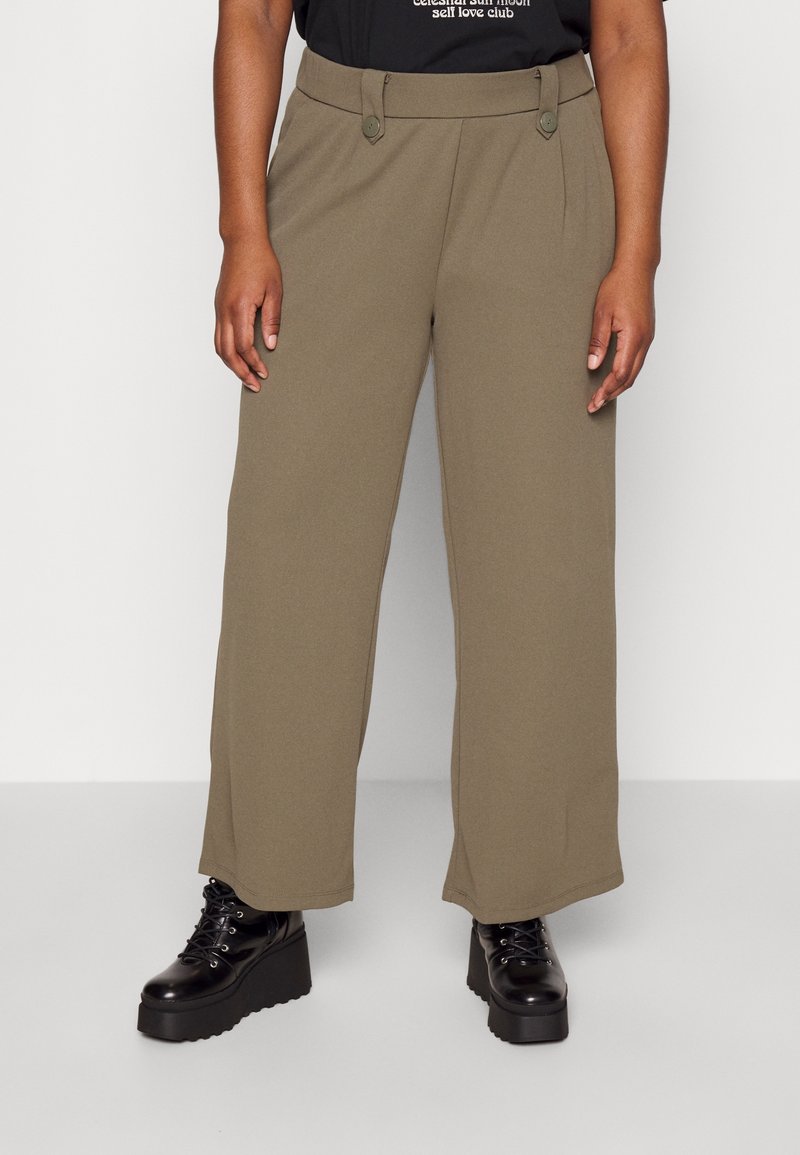 Personne portant un pantalon ample vert olive associé à des bottes à plateformes noires à lacets sur un fond uni.