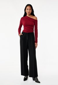 Burgundy off-shoulder langærmet bluse sat sammen med højtaljede sorte vidde bukser og spidse sorte ankelstøvler. Glat tekstur.