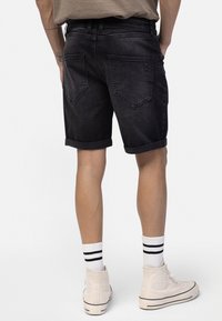 Person wearing black denim shorts, beige high-top sneakers with rhinestone design, and white socks with black stripes, standing on white background.