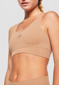 Nude sportinis liemenukas, pagamintas iš minkštos, tamprios medžiagos, turintis apvalų iškirpimą, plačias petnešas ir subtilų logotipo detalę centre.