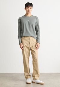 Langärmliges graues Shirt mit "BOSS"-Logo, beigen Hosen und weißen Sneakern. Lässiges Design mit lockerer Passform und glatter Textur.
