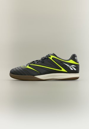 Chaussure de sport d'intérieur noire et jaune néon avec un design à lacets et une semelle en gomme, affichée sur un fond neutre.