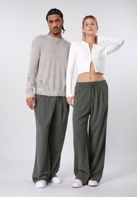 Szürke kötött pulóver kopottas részletekkel, olívazöld, finoman függőleges csíkozású, húzózsinóros nadrággal párosítva. Fehér sportcipő.