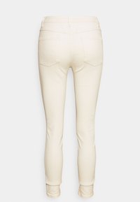 Crème-kleurige skinny jeans met een gladde textuur, voorzien van achterzakken en een subtiele omslag aan de zoom. Eenvoudig en veelzijdig ontwerp.