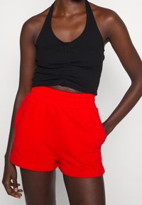 Haut court noir côtelé à col halter avec un détail froncé à l'avant, associé à un short à taille élastique rouge. Les deux sont fabriqués en tissu doux et léger.