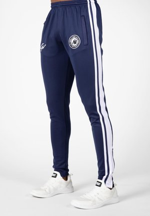 Navy athletic pants with white side stripes, elastic waistband, and pockets; features a round logo on the left thigh.