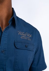 Korte mouwen marineblauw shirt van katoen met een button-down kraag, voorzien van twee voorzakken en een geborduurd logo in goud.