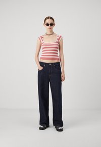 Débardeur rayé rose et blanc à col carré, associé à un jean en denim bleu foncé ample et des chaussures noires à semelles larges.