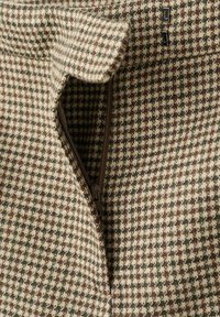 Primer plano de tela de espiga que muestra un zipper marrón parcialmente abierto y dos paradas de zipper negras en una tela texturizada.