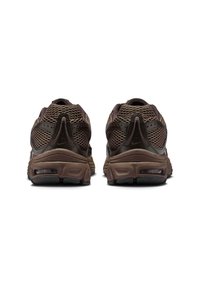 Bruna träningsskor med ovandel i mesh och vadderad krage, utrustade med en tjock gummisula och synlig luftdämpning vid hälen.