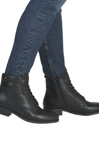 Bottines en cuir noir avec lacets et fermeture éclair sur le côté. Talon bas et texture lisse. Portées avec un jean bleu foncé.