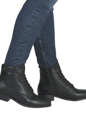 Bottines en cuir noir avec lacets et fermeture éclair sur le côté. Talon bas et texture lisse. Portées avec un jean bleu foncé.