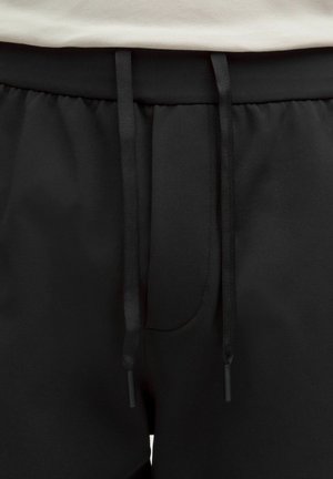 Černé sportovní šortky s texturovaným povrchem, vybavené stahovacím páskem a minimalistickým designem. Bez viditelných log nebo vzorů.