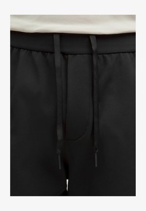 Čierne športové šortky s textúrovaným povrchom, sťahované v páse pomocou šnúrky, s minimalistickým dizajnom. Bez viditeľných log alebo vzorov.