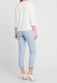Top bianco a tre quarti, jeans blu chiaro e scarpe con tacco bianche. Tessuto morbido, design aderente, con una silhouette semplice e pulita.