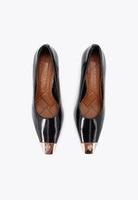 Ballerines en cuir verni noir avec un bout pointu et un capuchon métallique. L'intérieur est doublé d'un tissu marron matelassé. Marque visible sur la semelle intérieure.