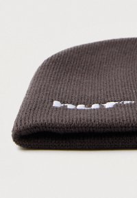 Sötétszürke, kötött sapka, részben látható fehér hímzett felirattal, sima fehér felületen.