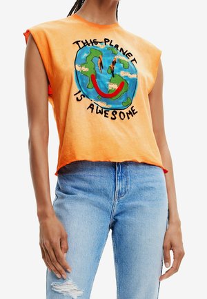 Osoba w pomarańczowej koszulce bez rękawów z kolorową grafiką ziemi i tekstem "This planet is awesome,", zestawiona z jasnoniebieskimi podartymi dżinsami.