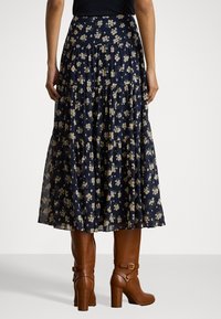 Gonna floreale navy con design a strati, caratterizzata da un leggero motivo floreale in oro. Abbinata a stivali con tacco marroni con cinturini alla caviglia.