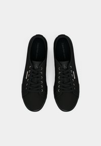 Crni platneni sneakers s okruglim prstima, ravnim vezicama i platnenim okovima. Imaju suptilan logo na jeziku i teksturiranu potplat za bolje prianjanje.