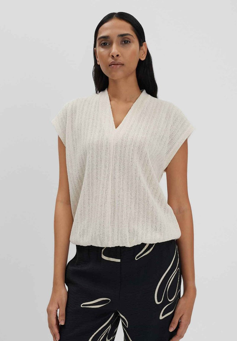 Licht beige gebreide top met een V-hals, korte mouwen en een gestructureerd streepmotief. Draag het met zwarte broeken met abstracte witte patronen.