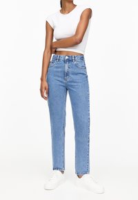 Vaqueros de tiro alto azul claro con corte recto, diseño de cinco bolsillos y lavado desgastado, combinados con una camiseta blanca ajustada de manga corta.