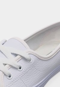 Chaussure décontractée en cuir blanc avec des lacets blancs et des coutures détaillées le long du côté et autour des œillets.