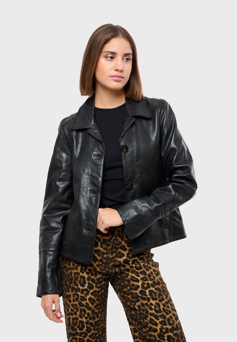 Černá koženková bunda s klasickým límcem, zapínáním na knoflíky a hladkým povrchem; nošena přes kalhoty s leopardským vzorem pro kontrast.