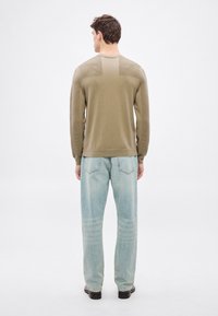 Lekki sweter w oliwkowej zieleni z fakturowanym tyłem, ściągaczami przy mankietach i dole. Połączony z luźnymi jasnoniebieskimi jeansami oraz czarnymi butami.