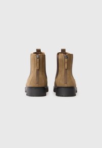 Barna velúr bokacsizmák fekete gumitalppal, melyek kétoldali cipzárral és bordázott díszítéssel rendelkeznek az egyszerű felvétel érdekében.