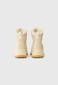 Κρέμα χρώματος μπότες με χνουδωτή εσωτερική επένδυση και υφή εξωτερικά. Διαθέτουν λογότυπο και αντίθετο καουτσούκ από καουτσούκ με γεύση γκουμ.