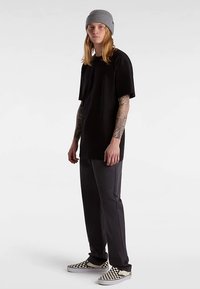 Zwart t-shirt met korte mouwen, grijze gebreide muts, donkergrijze broek en zwart-witte geruite instapsneakers.