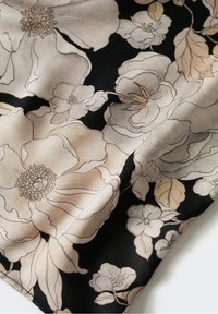 Tissu noir avec de grands motifs floraux beige et gris clair comprenant des pétales et des feuilles détaillés.