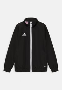 Zwarte Adidas trainingsjack met een hoge kraag, volledige ritssluiting, wit logo en elastische manchetten en zoom. Twee zijzakken zichtbaar.
