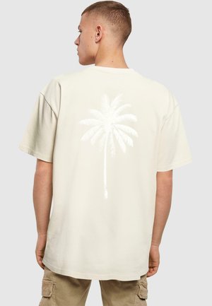 Beige oversized T-shirt med et hvidt palme-træ grafik på bagsiden. Korte ærmer, rund halsudskæring, bomulds materiale, afslappet design.