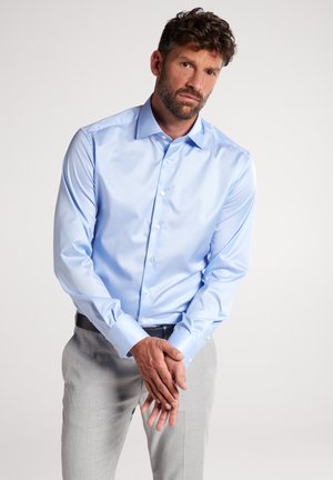Chemise habillée bleu clair à manches longues en tissu coton lisse, dotée d'un col classique et d'une fermeture à boutons, associée à un pantalon gris clair.