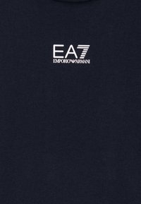 Tamno plavi pamučni majica s bijelim logotipom koji sadrži tekst "EA7" i "Emporio Armani". Jednostavan dizajn, kratki rukavi, okrugli izrez.