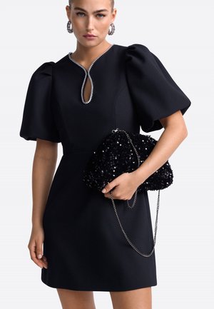 Svart klänning med puffärmar och nyckelhålsutskärning, prydd med rhinestones. Matchad med en svart paljettväska med kedja.