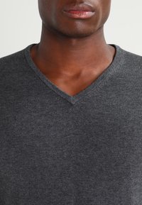 Mörkgrå V-ringad tröja gjord av mjukt stickat tyg, med en slät yta och diskret sömnad längs halsringningen.