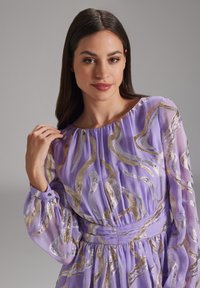 Robe en chiffon violet avec des motifs ondulés dorés, manches ballon longues, encolure froncée et taille ajustée.