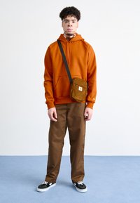 Orange hooded sweatshirt, brown pants, black sneakers, and a brown corduroy crossbody bag with a logo. Simple, casual outfit.