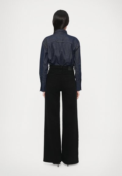 Tmavomodrá rifľová košeľa s golierom a dlhými rukávmi, kombinovaná s čiernymi širokými nohavicami s vysokým pásom a lodičkovými opätkami.