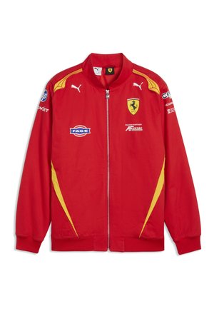Czerwona kurtka wyścigowa Ferrari z żółtymi akcentami, logo Puma, zamkiem z przodu i wieloma naszywkami sponsorów na klatce piersiowej i rękawach.