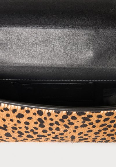 Sac à imprimé léopard ouvert montrant un intérieur en cuir noir lisse avec des coutures visibles le long des bordures.