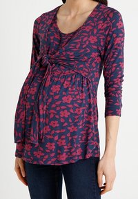 Äitiysfarkku, tummansininen, jossa on vaaleanpunaisia kukkakuvioita, pitkät hihat ja solmittava yksityiskohta edessä. Pehmeä kangas, jossa on rento istuvuus mukavuutta varten.