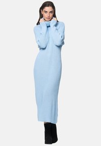 Helles blaues geripptes Strickkleid mit hohem Kragen, langen Ärmeln und bodenlanger Ausführung, kombiniert mit schwarzen Knöchelstiefeln.
