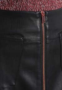 Musta nahkahame, jossa on teksturoitu pinta, ja siinä on ruusukultainen vetoketju sekä kaksi sivutaskua. Yllä oleva kangas on viininpunaisissa sävyissä neulottua.